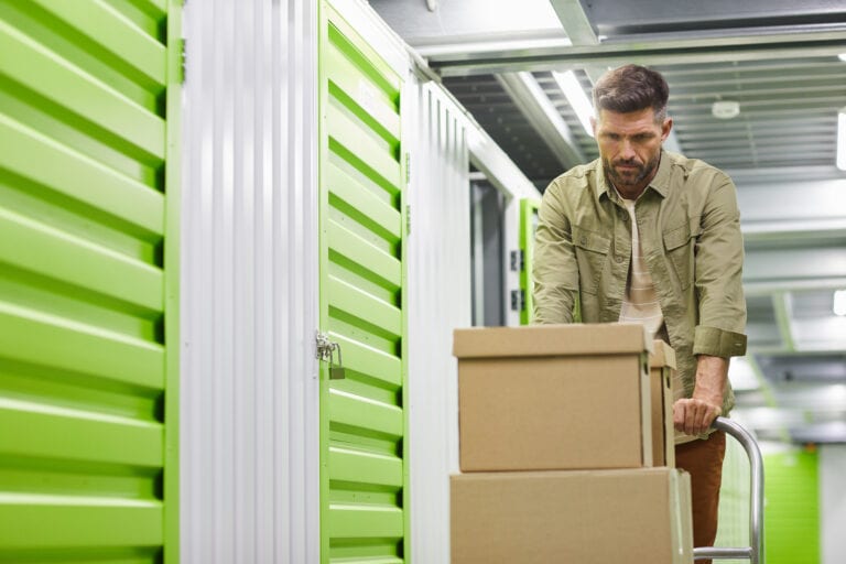 Waist up portrait of handsome bearded man loading cart with cardboard boxes into self storage unit, copy space