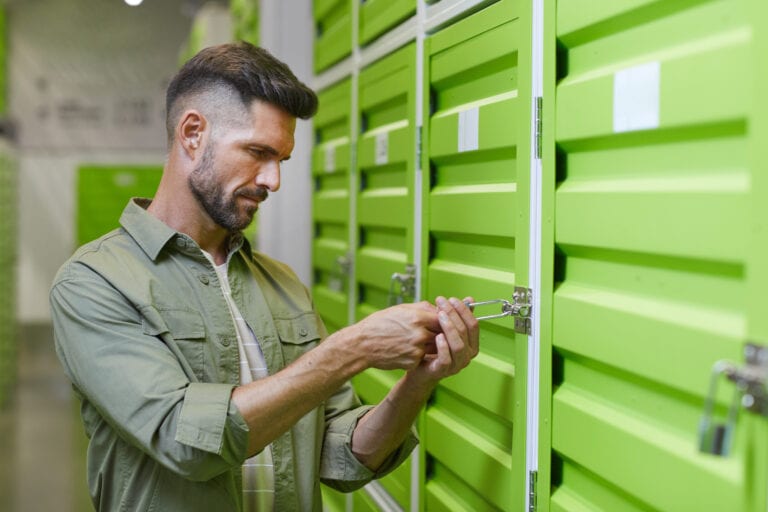 Waist up portrait of handsome bearded man opening padlock on door of self storage unit , copy space