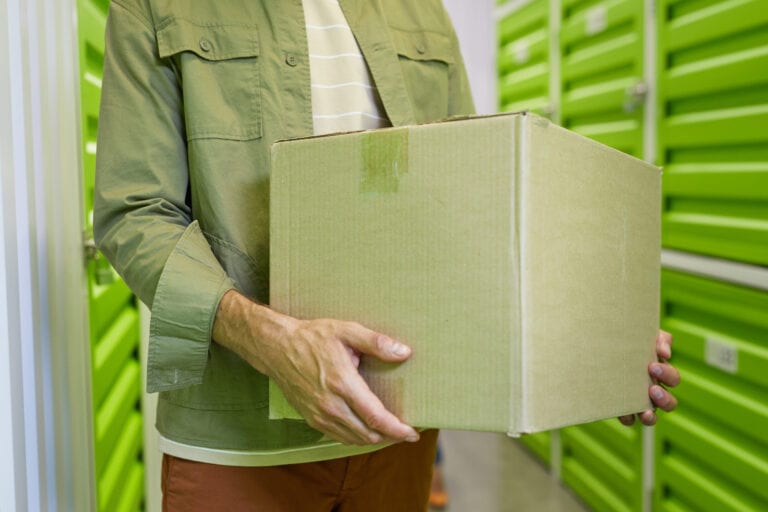 Cropped shot of unrecognizable man holding cardboard box standing in self storage facility, copy space
